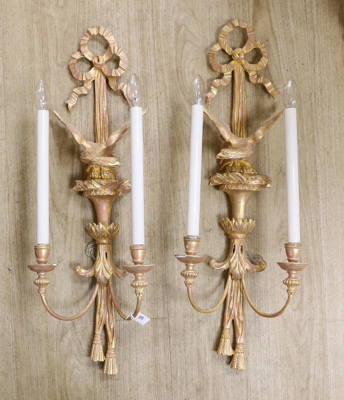 A pair of Louis XVI style carved giltwood wall lights, with ribbon crests and winged eagle stems, over tasselled bases, height 79cm